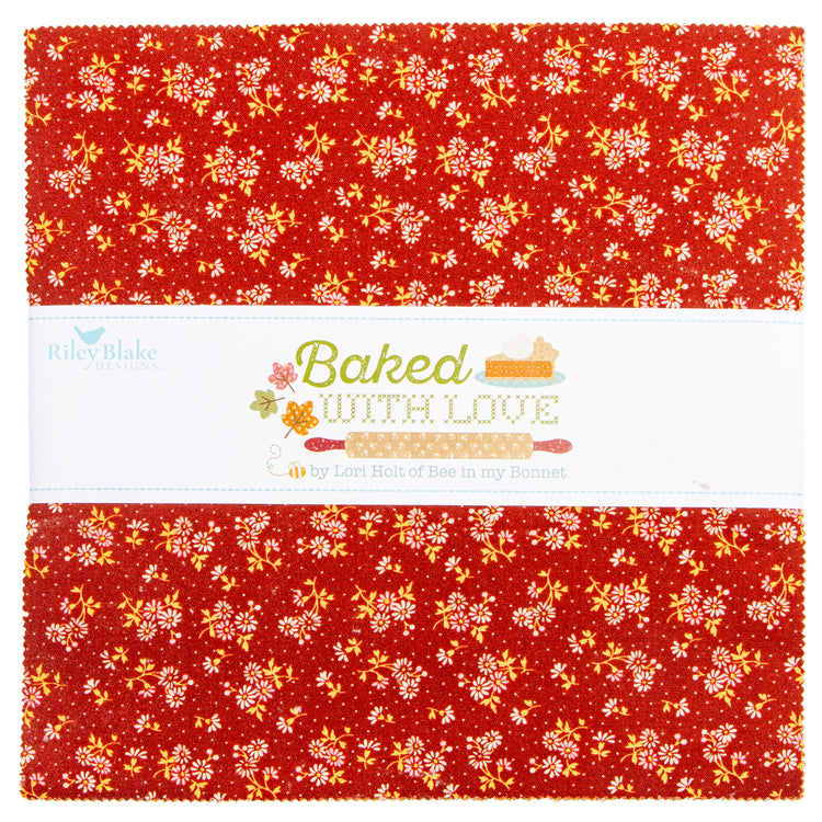 A folded fabric bundle with a red background and a white center band printed with the text 'Baked WITH LOVE' and 'by Lori Hall of Bew in my Beecher.' The fabric has a repeating floral and leaf pattern in yellow, orange, and white.
