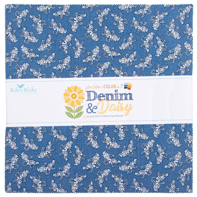 A folded fabric swatch with a blue denim-like background and a repeating white floral and scroll pattern, wrapped with a white paper label that reads Riley Blake Designs and Denim & Daisy.