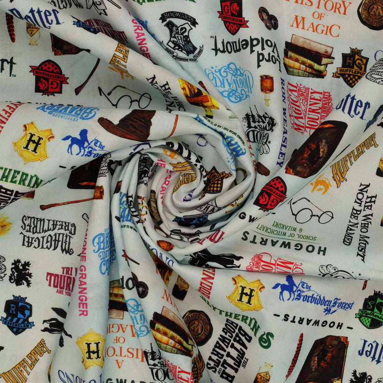 Pale blue Harry Potter fabric with multicolored words, house crests, books, potion bottles, wands and spectacles in a swirl.