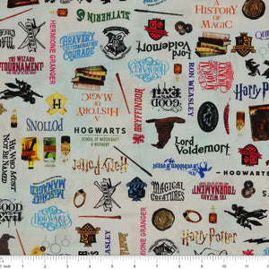 Pale blue Harry Potter fabric with multicolored words, house crests, books, potion bottles, wands and spectacles with ruler for scale.