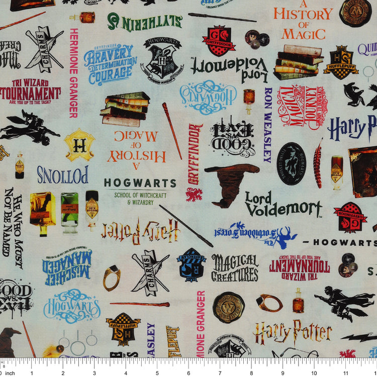 Pale blue Harry Potter fabric with multicolored words, house crests, books, potion bottles, wands and spectacles with ruler for scale.