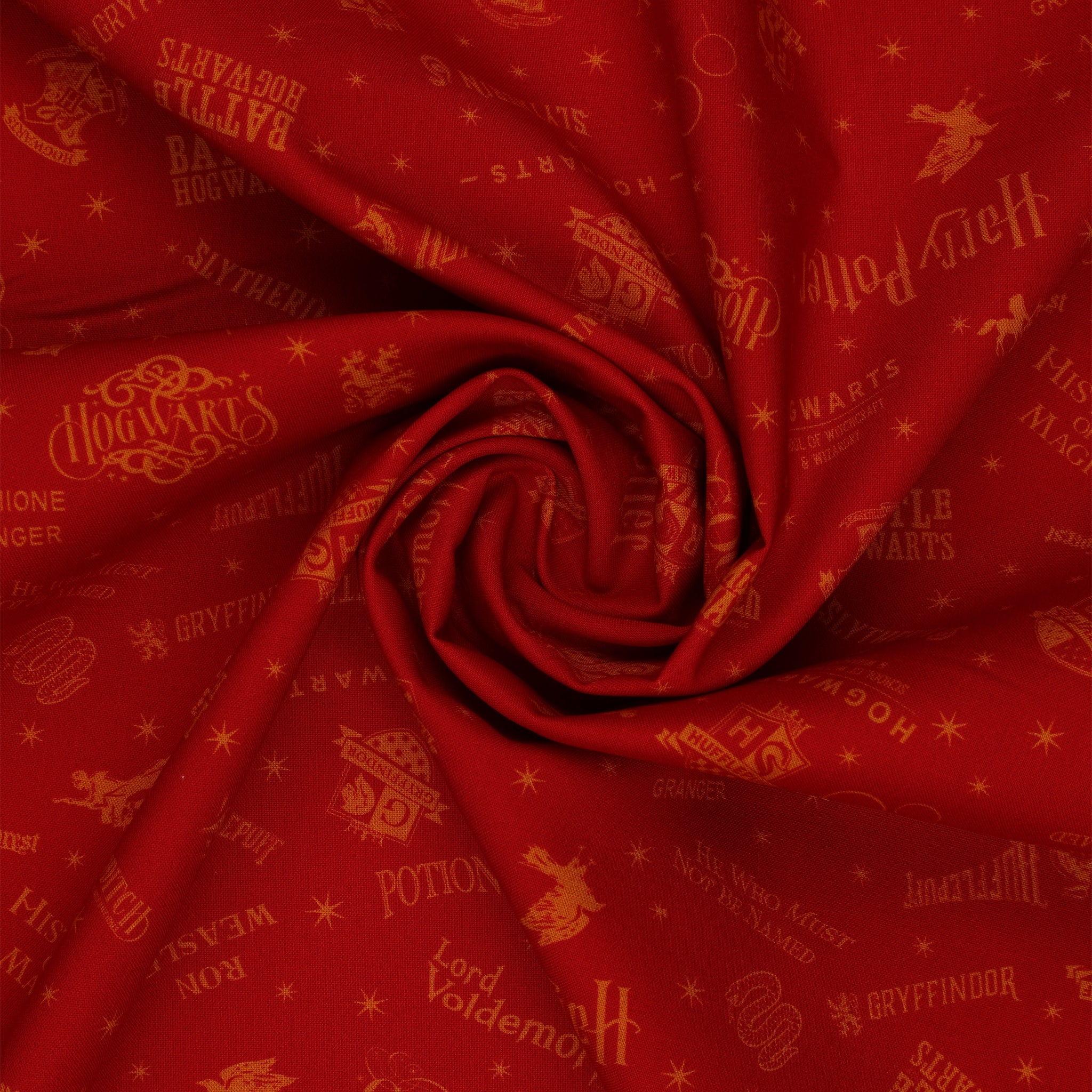 Red Harry Potter fabric with golden-yellow lettering, Hogwarts house shields and scattered stars in a swirl.