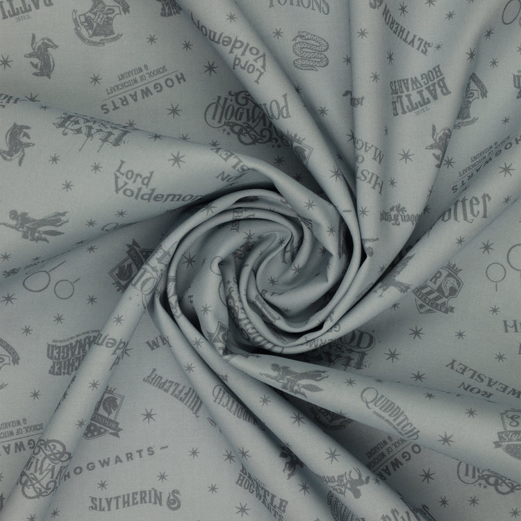 Light gray Harry Potter fabric with darker gray lettering, Hogwarts crests, magical icons and stars in a swirl.