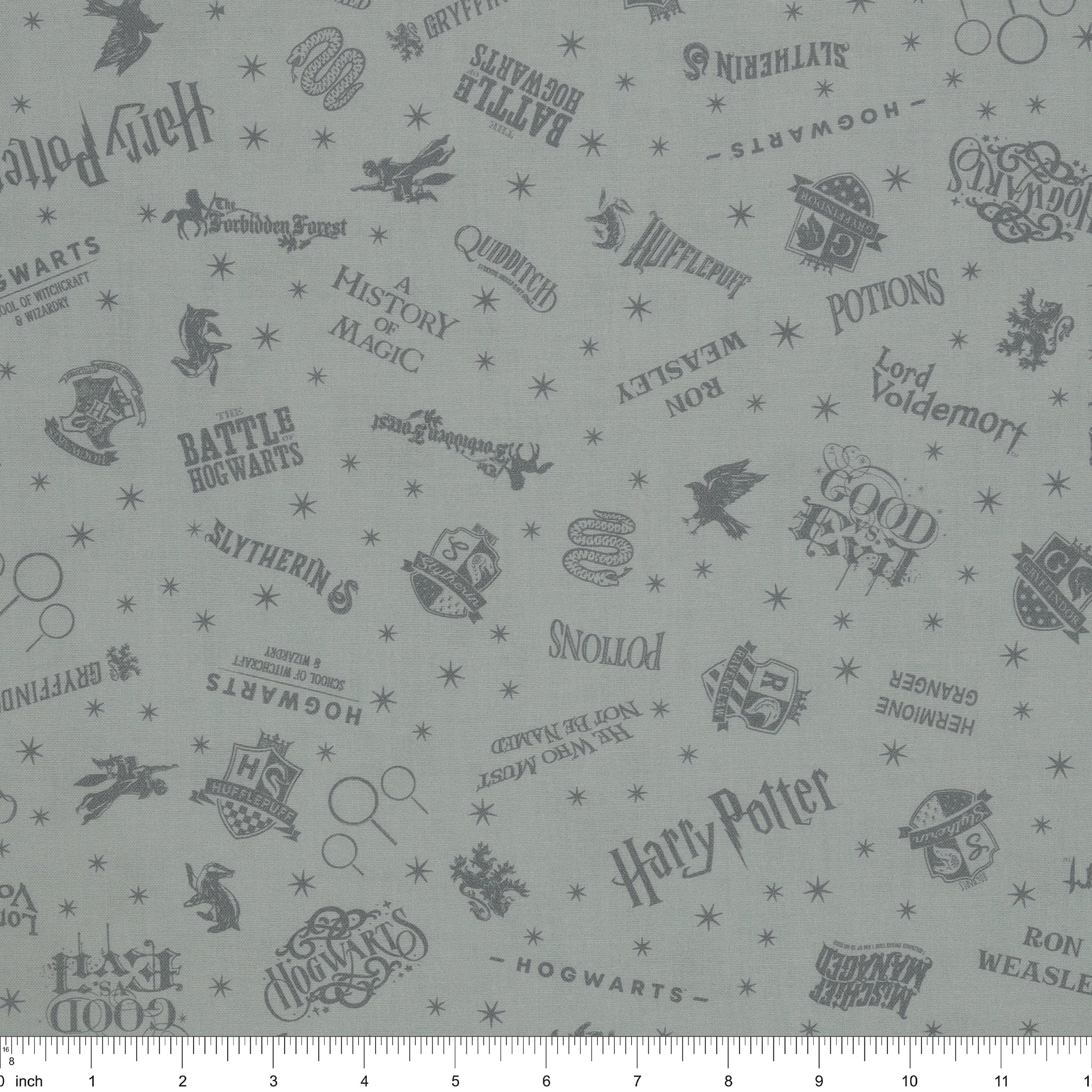 Light gray Harry Potter fabric with darker gray lettering, Hogwarts crests, magical icons and stars with ruler for scale.