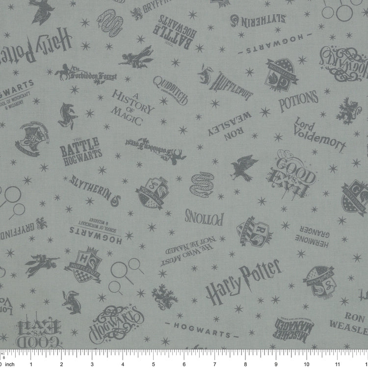 Light gray Harry Potter fabric with darker gray lettering, Hogwarts crests, magical icons and stars with ruler for scale.