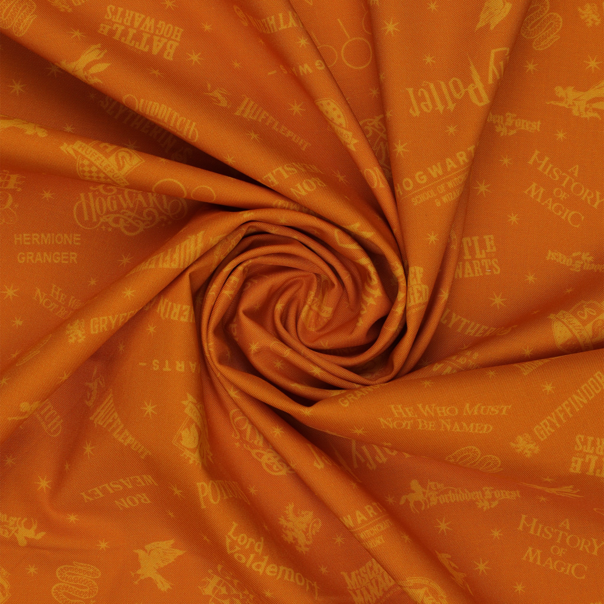 Amber-gold Harry Potter fabric with lighter golden words, house emblems and tiny starbursts in a swirl.