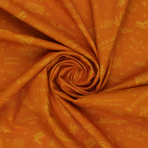 Amber-gold Harry Potter fabric with lighter golden words, house emblems and tiny starbursts in a swirl.