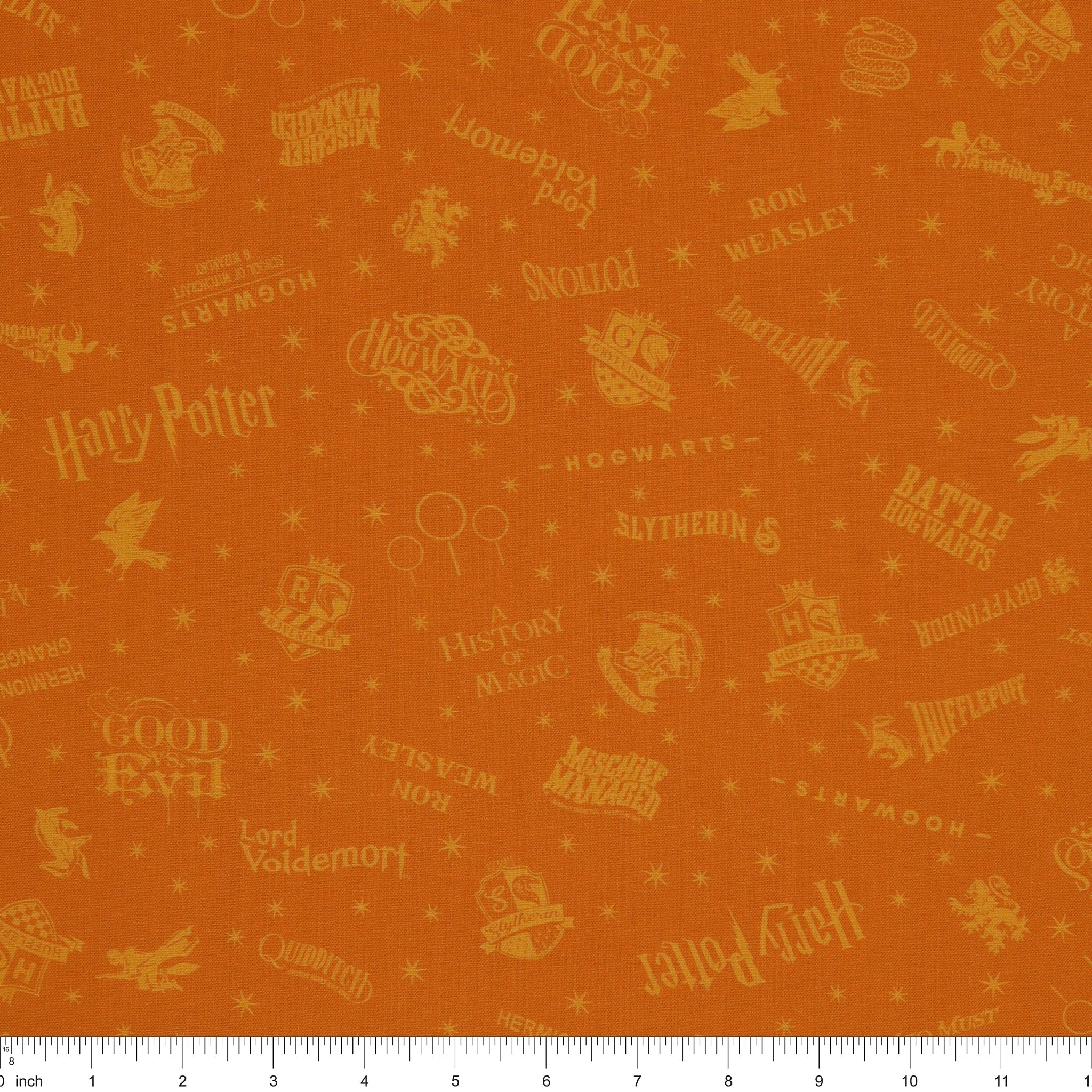 Amber-gold Harry Potter fabric with lighter golden words, house emblems and tiny starbursts with ruler for scale.