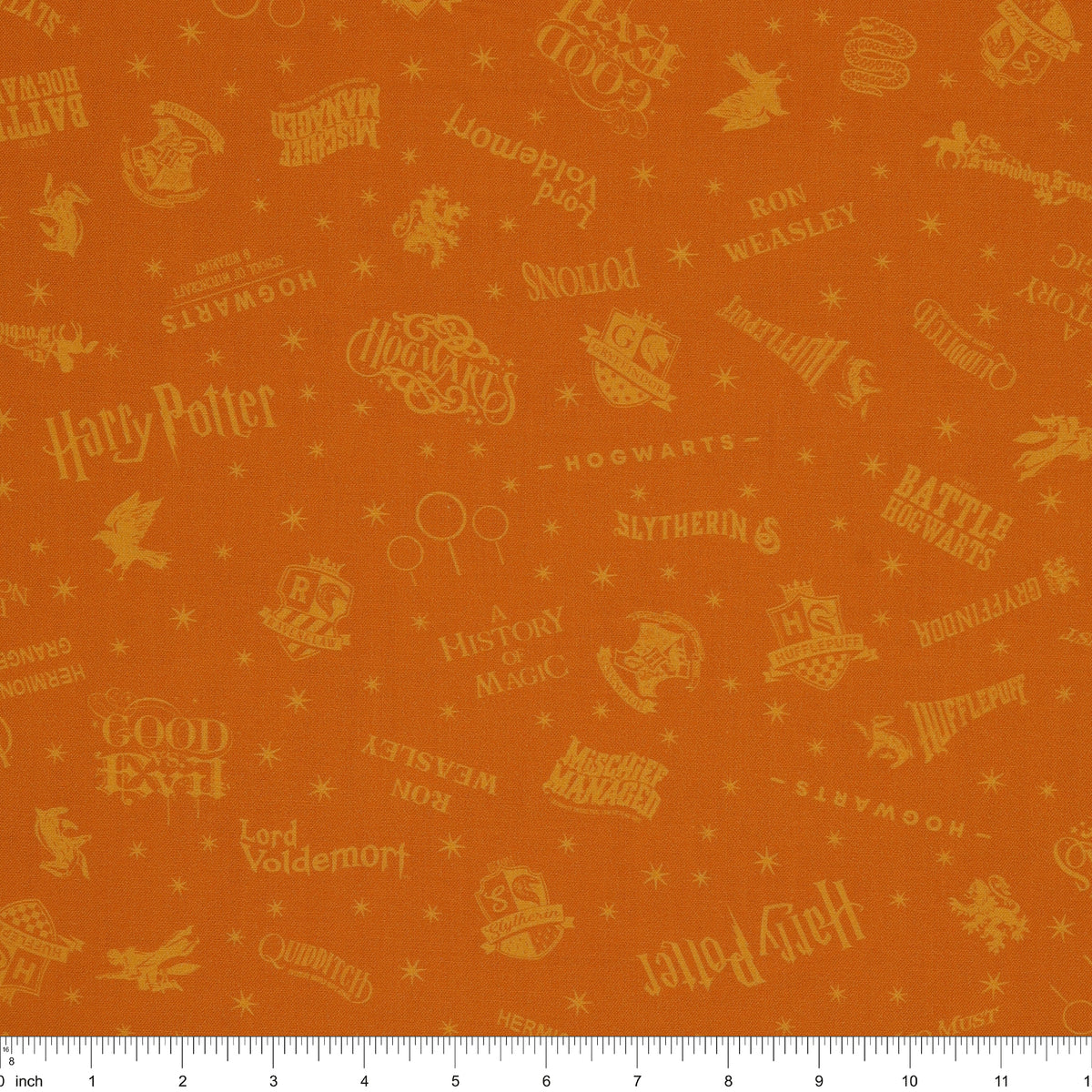 Amber-gold Harry Potter fabric with lighter golden words, house emblems and tiny starbursts with ruler for scale.