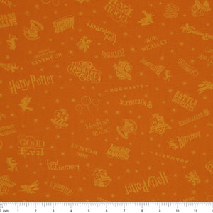 Amber-gold Harry Potter fabric with lighter golden words, house emblems and tiny starbursts with ruler for scale.