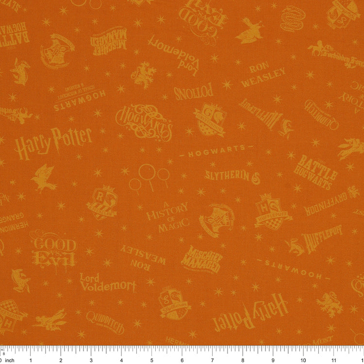 Amber-gold Harry Potter fabric with lighter golden words, house emblems and tiny starbursts with ruler for scale.
