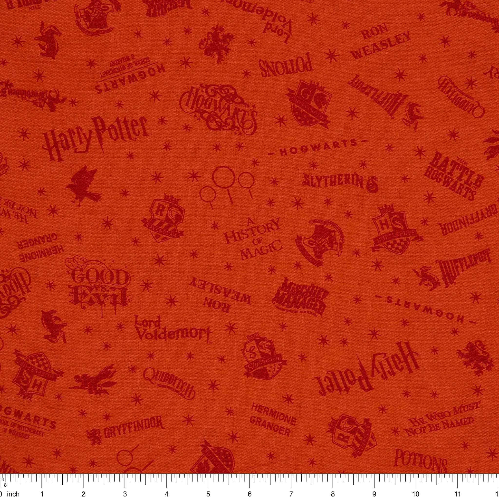 Orange Harry Potter fabric with rust-red words, Hogwarts house crests and scattered starbursts with ruler for scale.