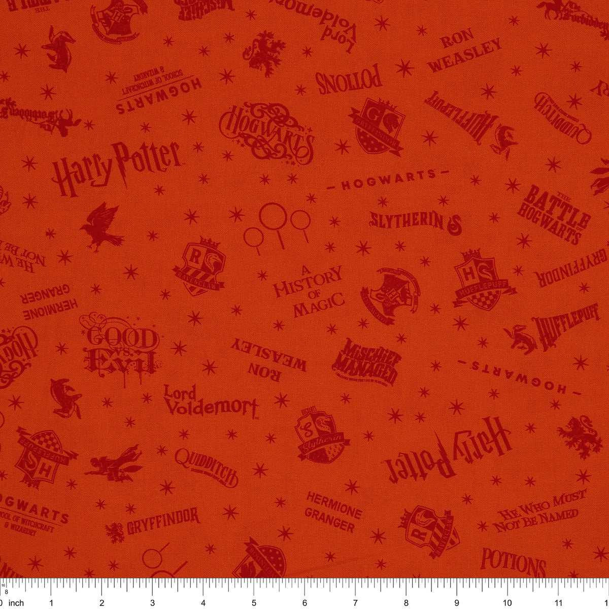 Orange Harry Potter fabric with rust-red words, Hogwarts house crests and scattered starbursts with ruler for scale.