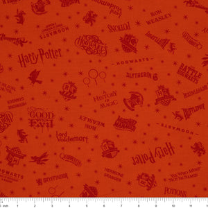 Orange Harry Potter fabric with rust-red words, Hogwarts house crests and scattered starbursts with ruler for scale.