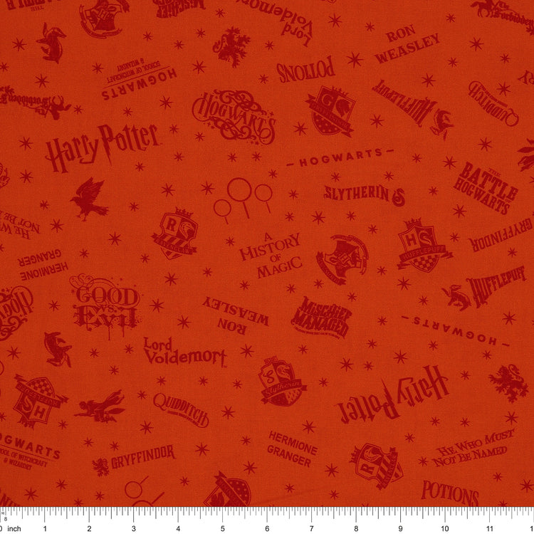 Orange Harry Potter fabric with rust-red words, Hogwarts house crests and scattered starbursts with ruler for scale.