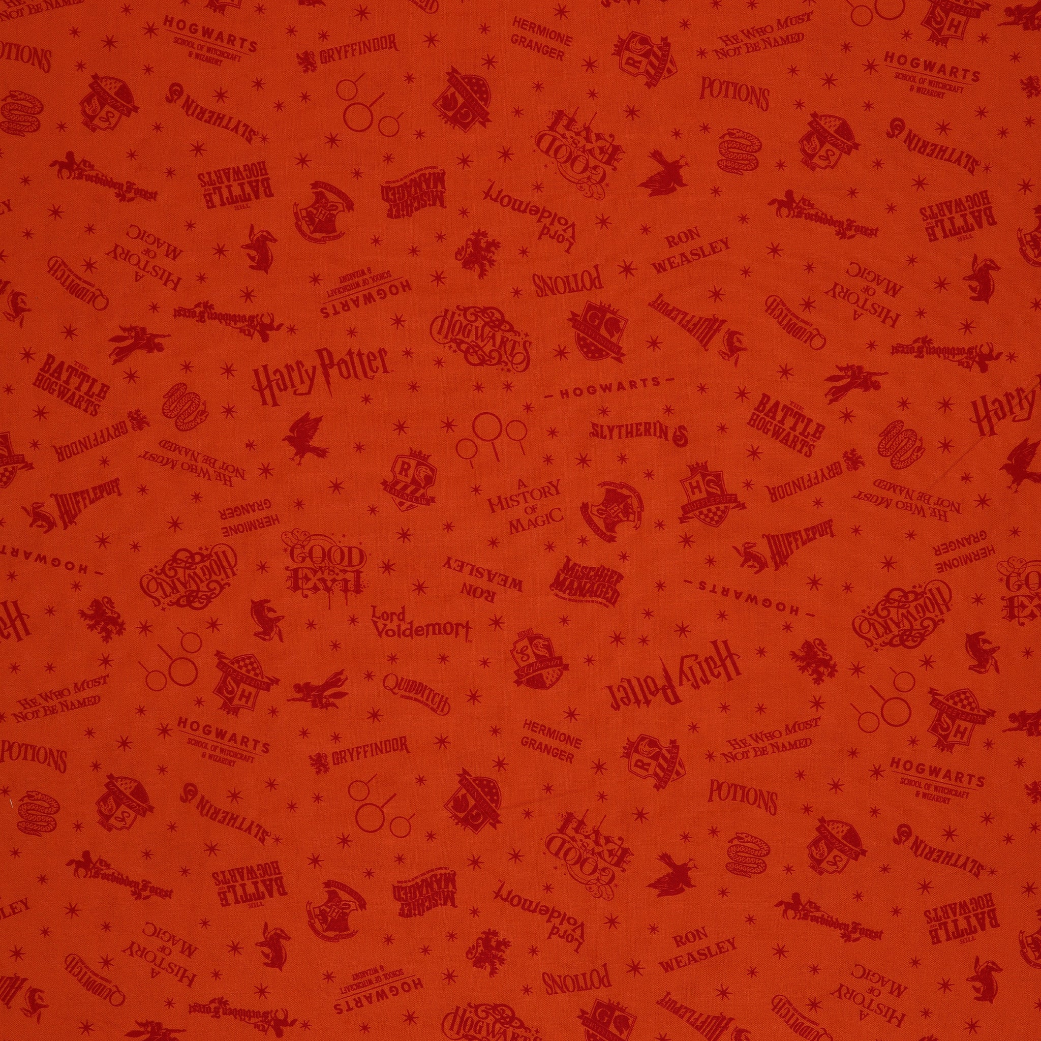 Orange Harry Potter fabric with rust-red words, Hogwarts house crests and scattered starbursts.