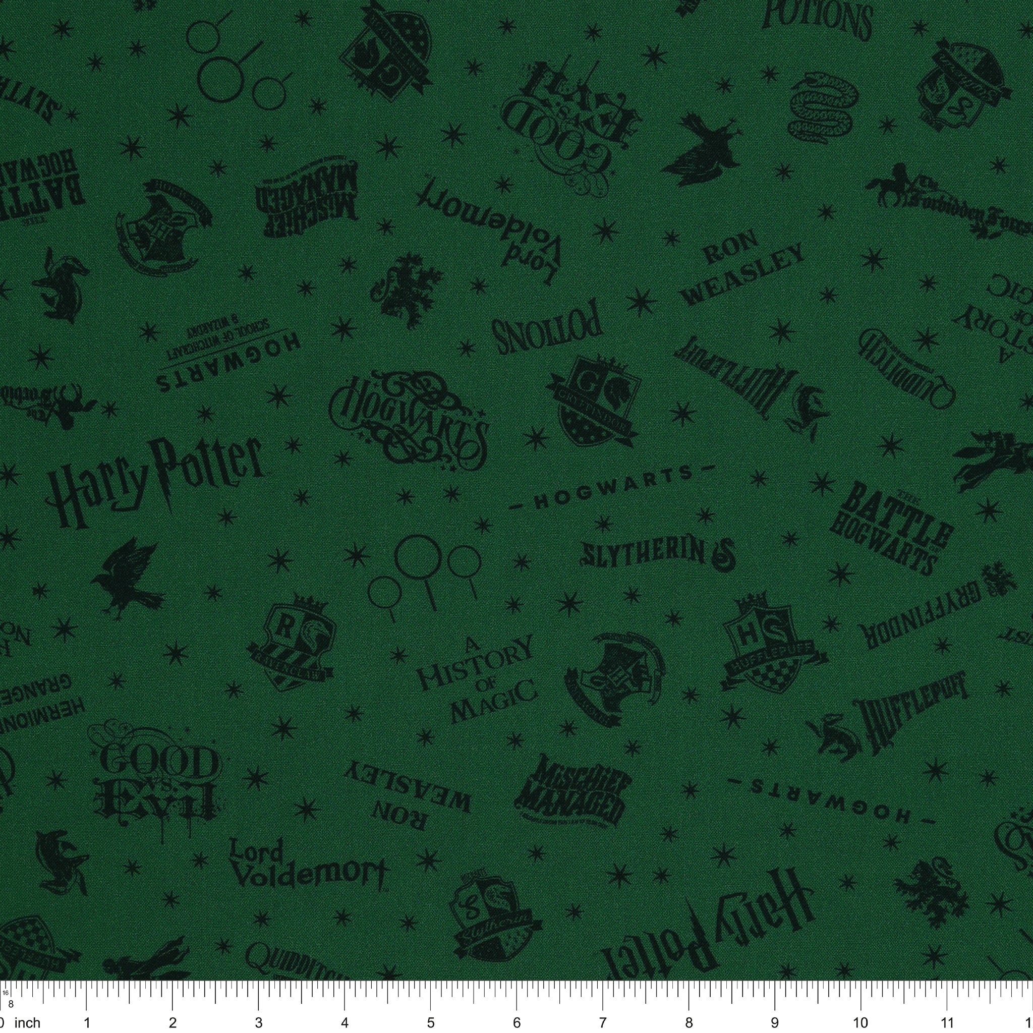 Dark green Harry Potter fabric with nearly black house crests, serpents, words and scattered stars with ruler for scale.