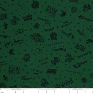Dark green Harry Potter fabric with nearly black house crests, serpents, words and scattered stars with ruler for scale.