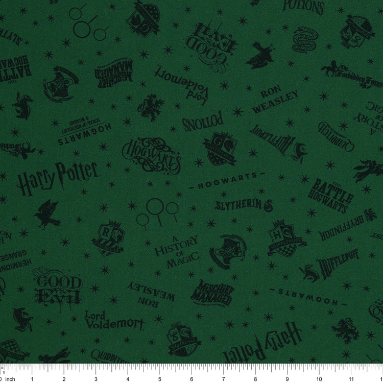 Dark green Harry Potter fabric with nearly black house crests, serpents, words and scattered stars with ruler for scale.