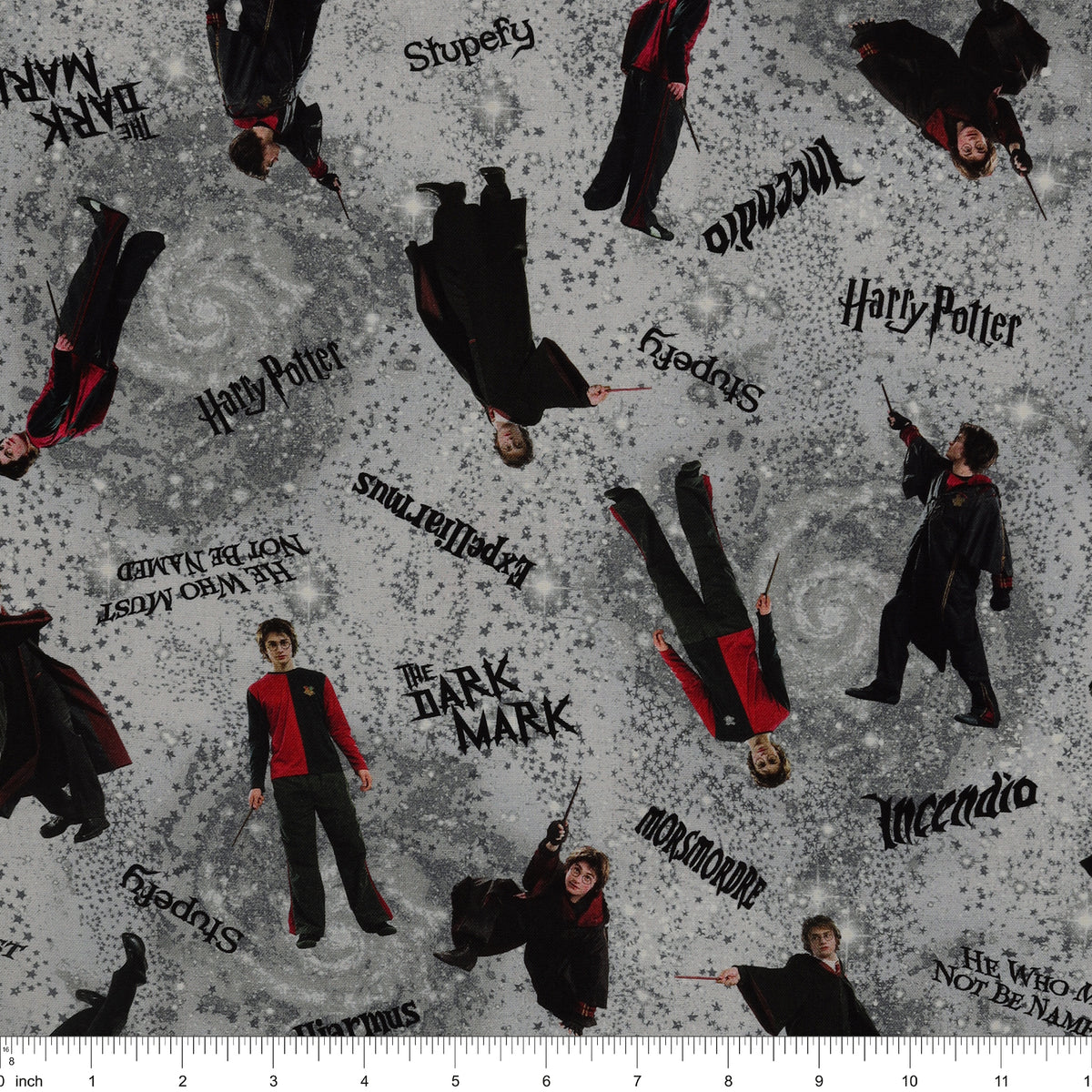 Gray Harry Potter fabric with wand-wielding figures, spell names, stars and smoky swirls with ruler for scale.