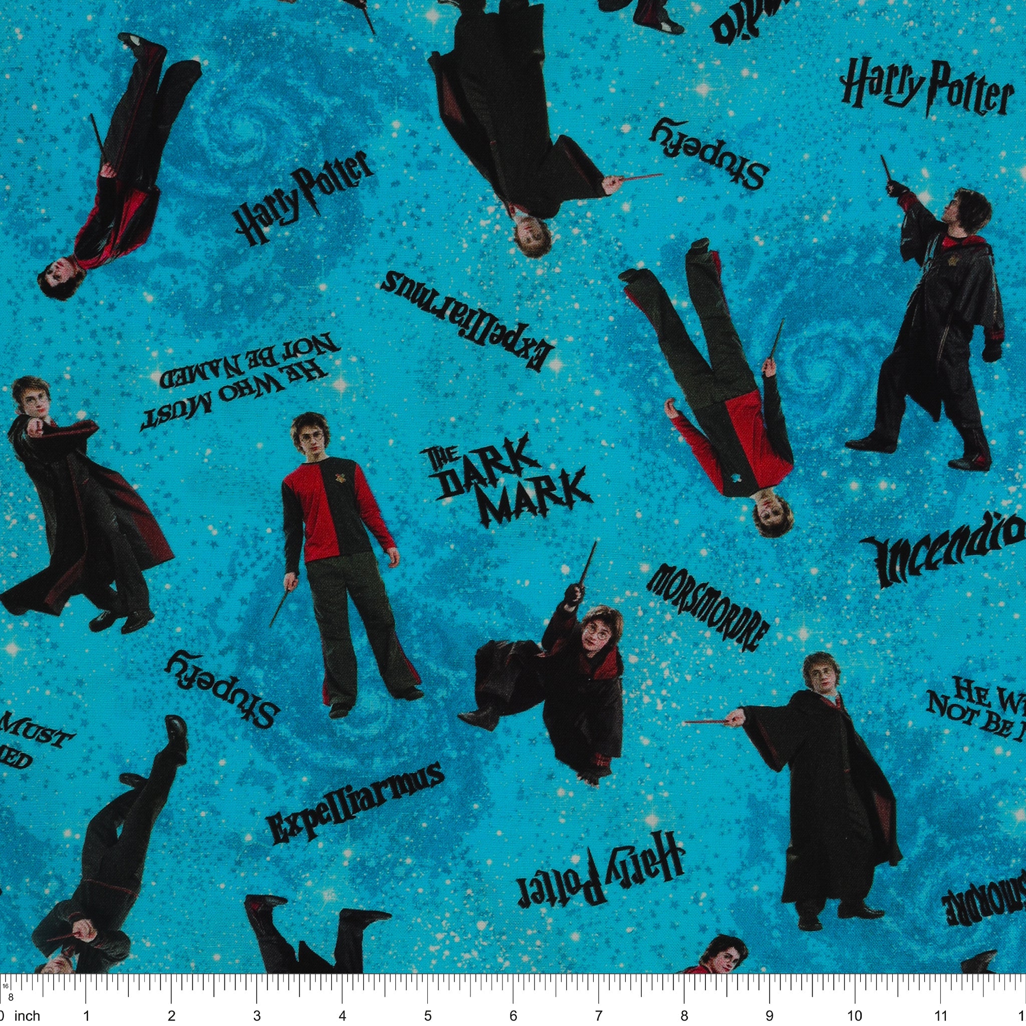 Turquoise Harry Potter fabric with robed figures, black spell lettering and scattered stars over blue swirls with ruler for scale.
