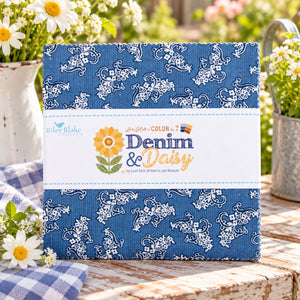 A fabric bundle wrapped with a white paper label placed on a wooden surface with flowers and a gingham cloth in a garden setting.