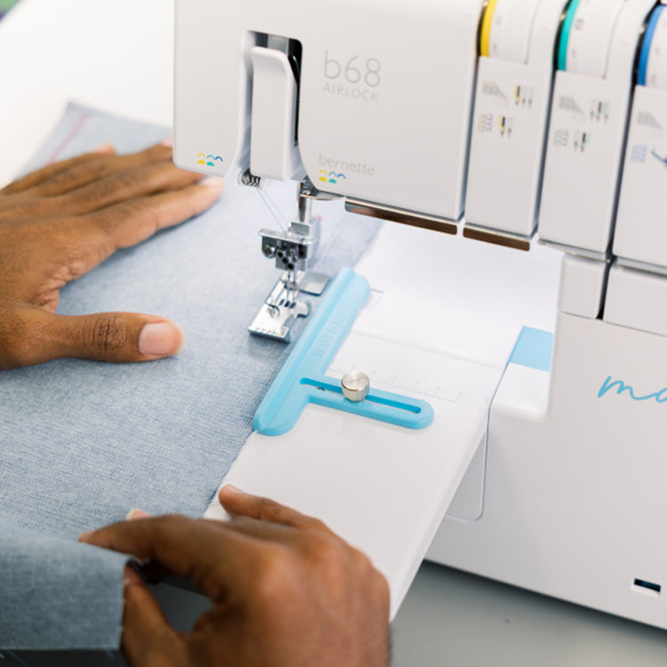 bernette b68 AIRLOCK Serger with blue adjustable fabric guide attachment while sewing denim fabric.