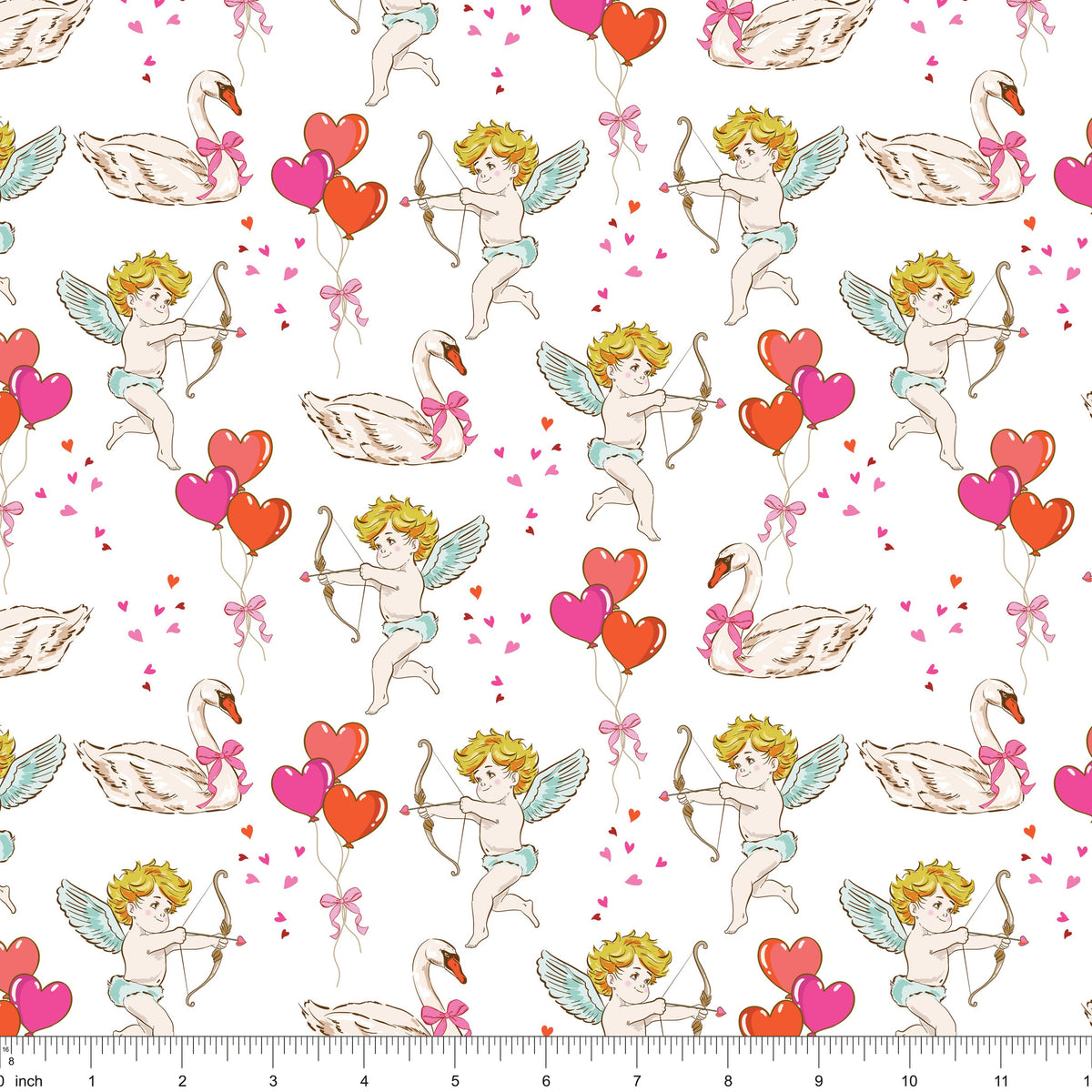 White fabric with cherubs drawing bows, swans and heart balloons, shown with ruler for scale