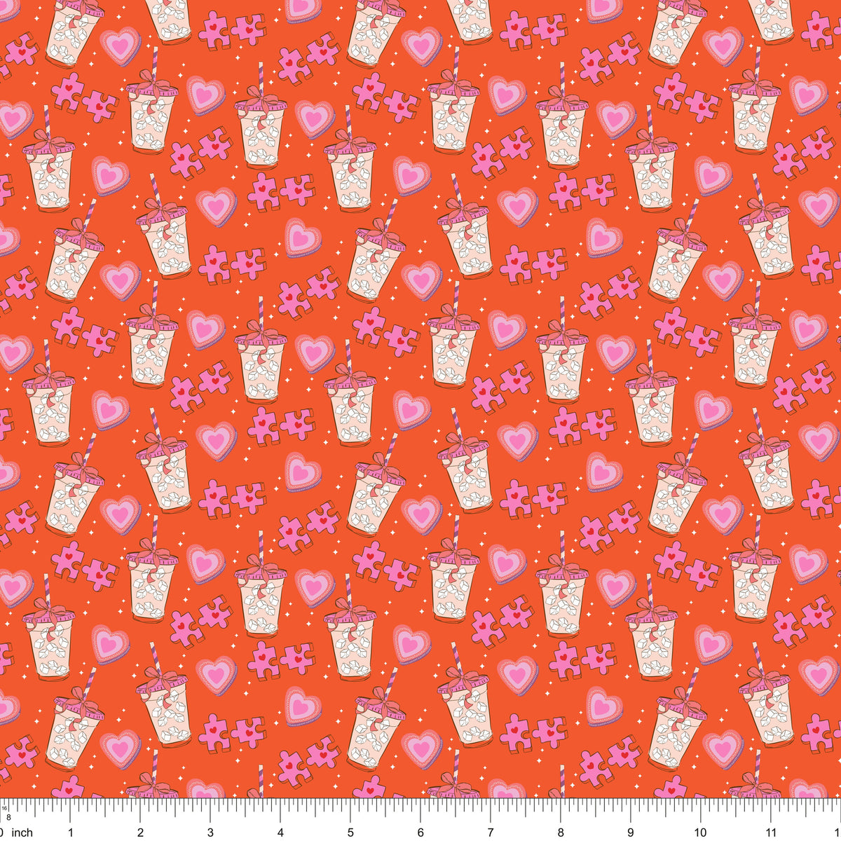 Orange fabric with iced drinks, pink hearts and puzzle pieces, shown with ruler for scale
