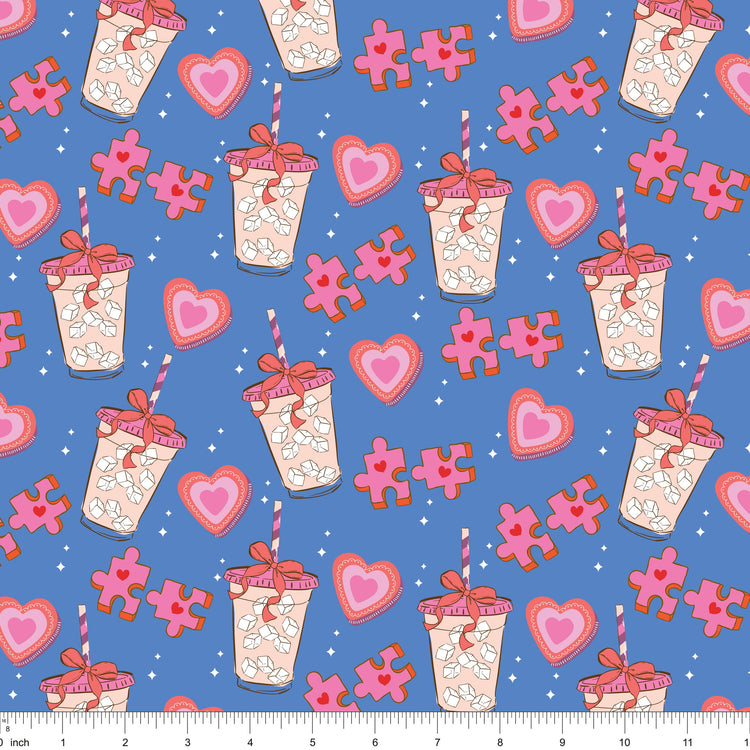 Blue fabric with iced drinks tied with bows, pink hearts and puzzle pieces, shown with ruler for scale