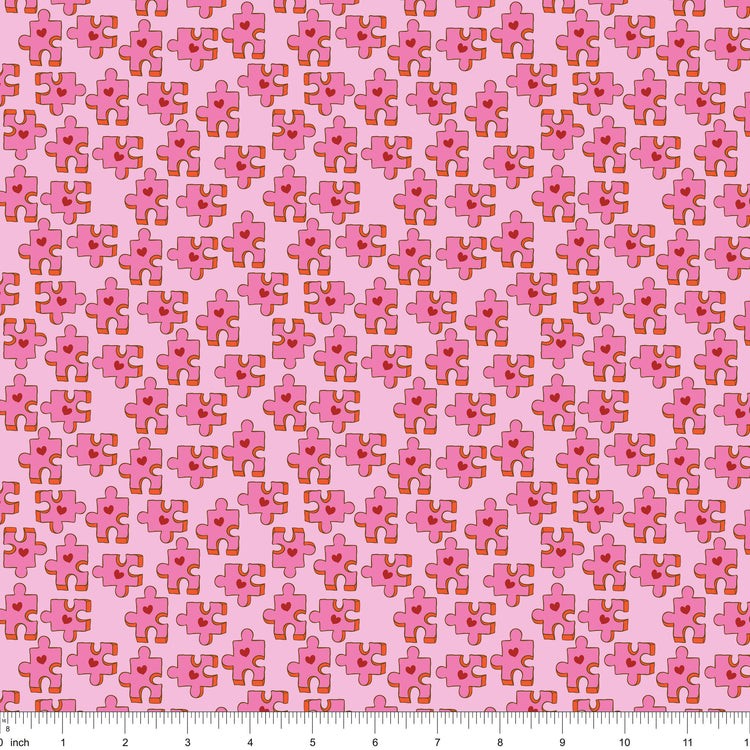 Pink fabric with puzzle pieces and red hearts, shown with ruler for scale