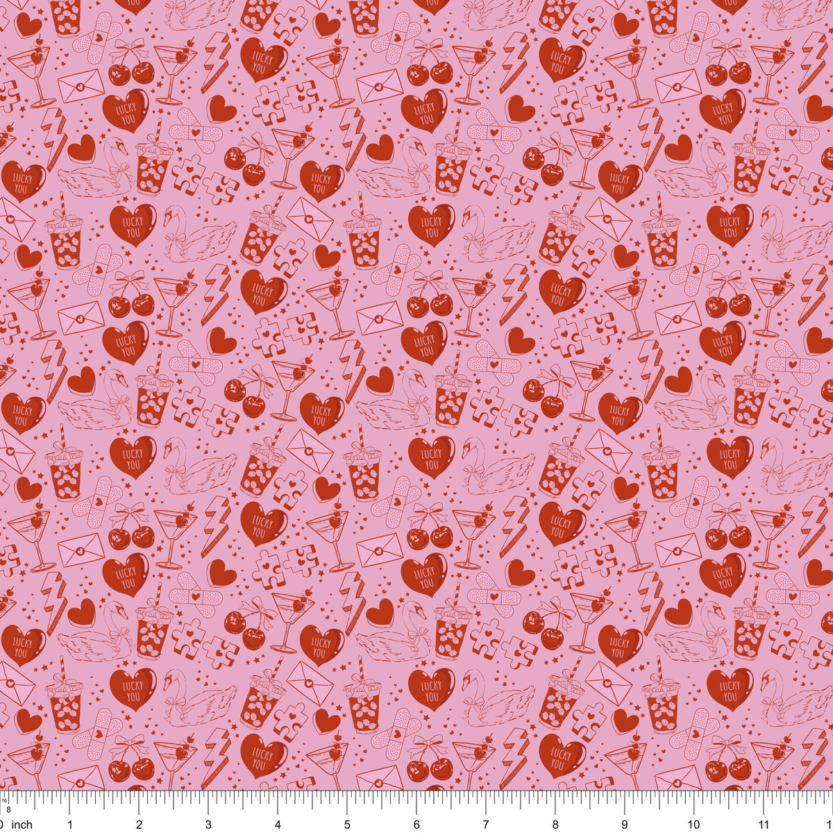 Pink fabric with red line drawings of hearts, swans, cocktails and Lucky You candy hearts, shown with ruler for scale