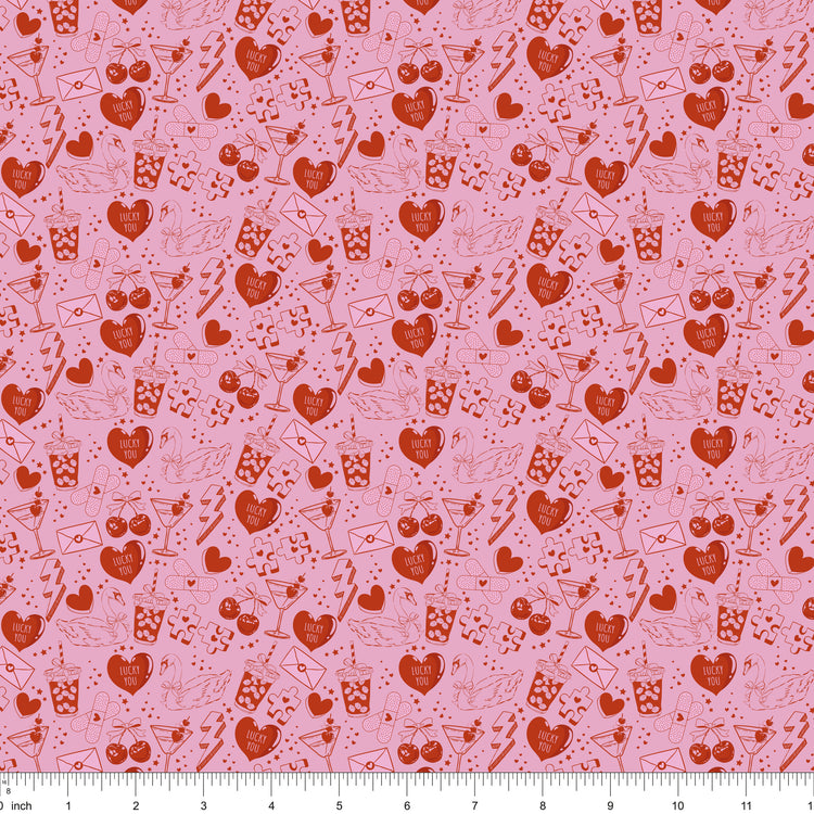 Pink fabric with red line drawings of hearts, swans, cocktails and Lucky You candy hearts, shown with ruler for scale