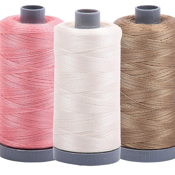 Three Aurifil 28wt Mako cotton thread spools in coral, ivory and taupe