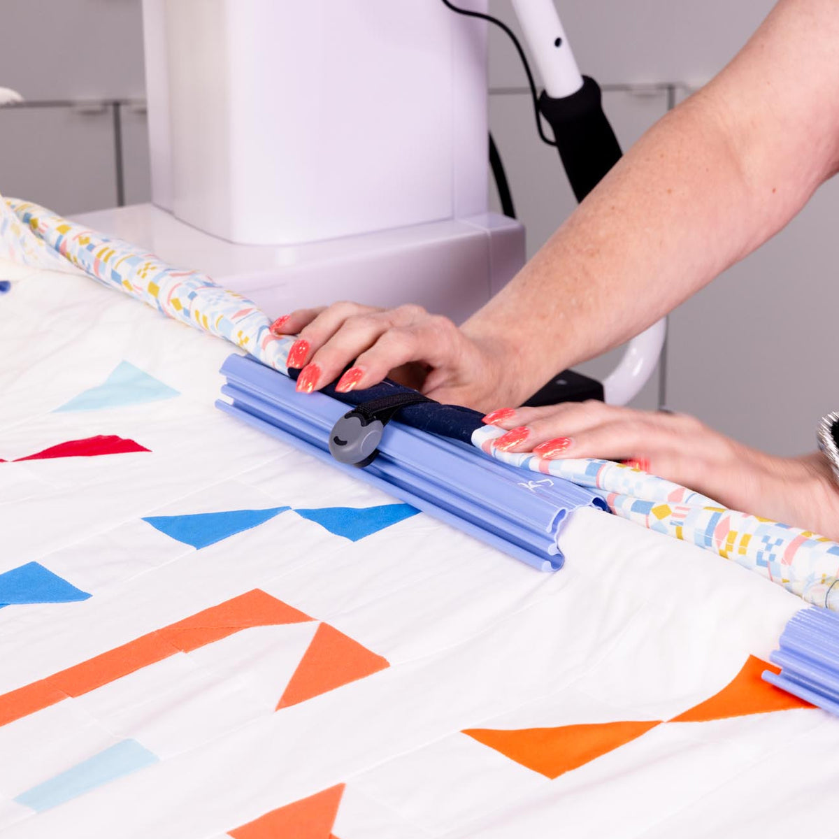 A close-up of a person using a blue quilting fabric clamp to fold a patterned fabric.