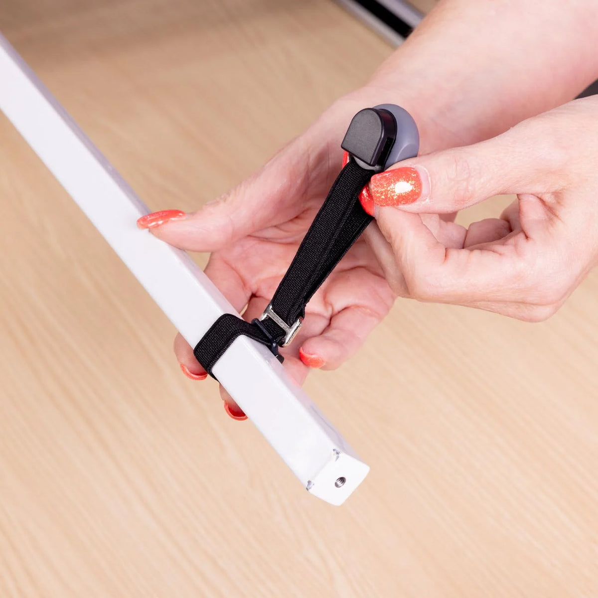 A close-up of a person's hands with orange glitter nail polish attaching a black elastic strap to a white bar.
