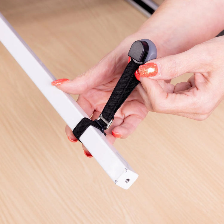 A close-up of a person's hands with orange glitter nail polish attaching a black elastic strap to a white bar.