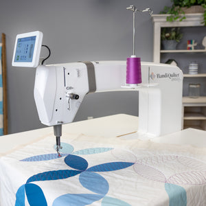 Handi Quilter Amara ST longarm quilting machine with touchscreen display and purple thread cone, stitching a modern blue and purple abstract quilt on a spacious sit-down quilting table.