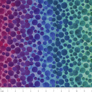 Bumbleberries Rainbow fabric with densely scattered watercolor dots over a bright ombre background blending red, pink, purple, blue, turquoise, green, yellow, and orange. Ruler for scale. 