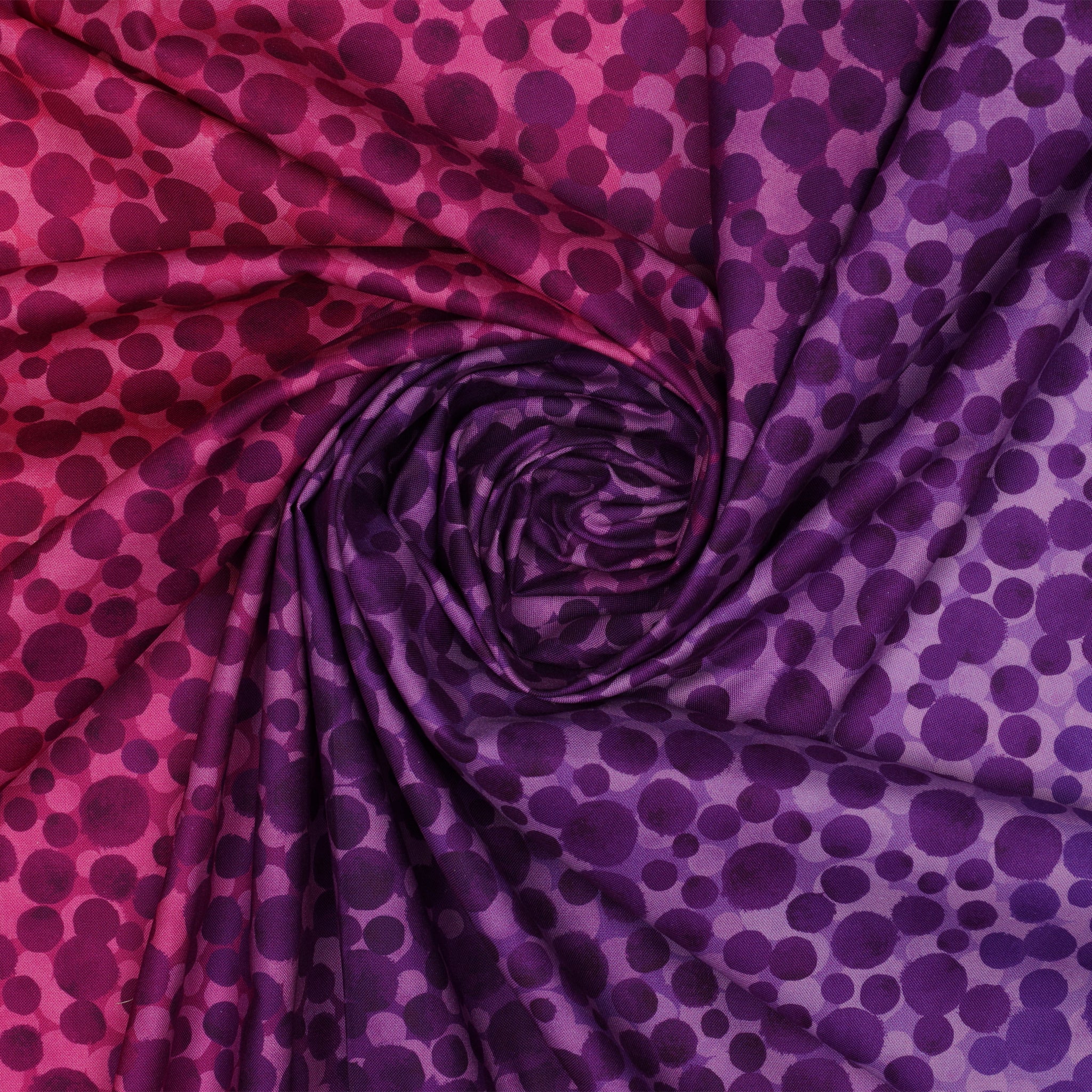 Bumbleberries Pinky Purple fabric gathered in a spiral, showcasing varying sizes of dark purple and plum-colored dots against pink and violet backgrounds.