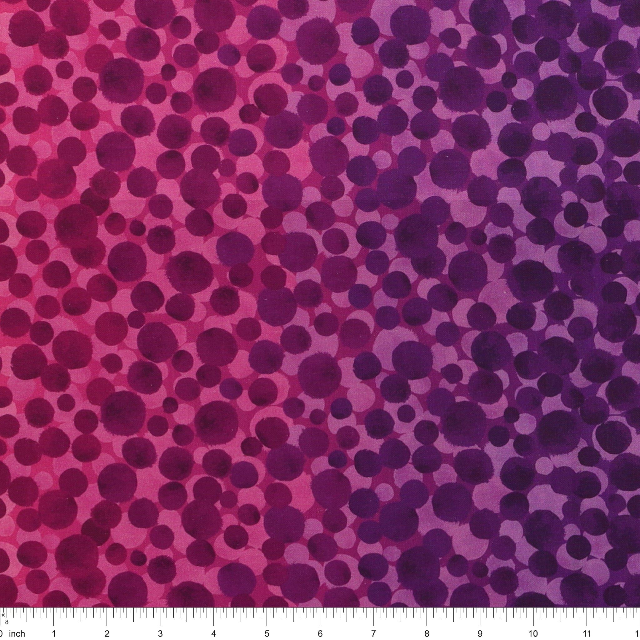 Bumbleberries Pinky Purple fabric with irregular dots in shades of magenta, plum, and violet over a pink-to-purple gradient background with a ruler for scale. 