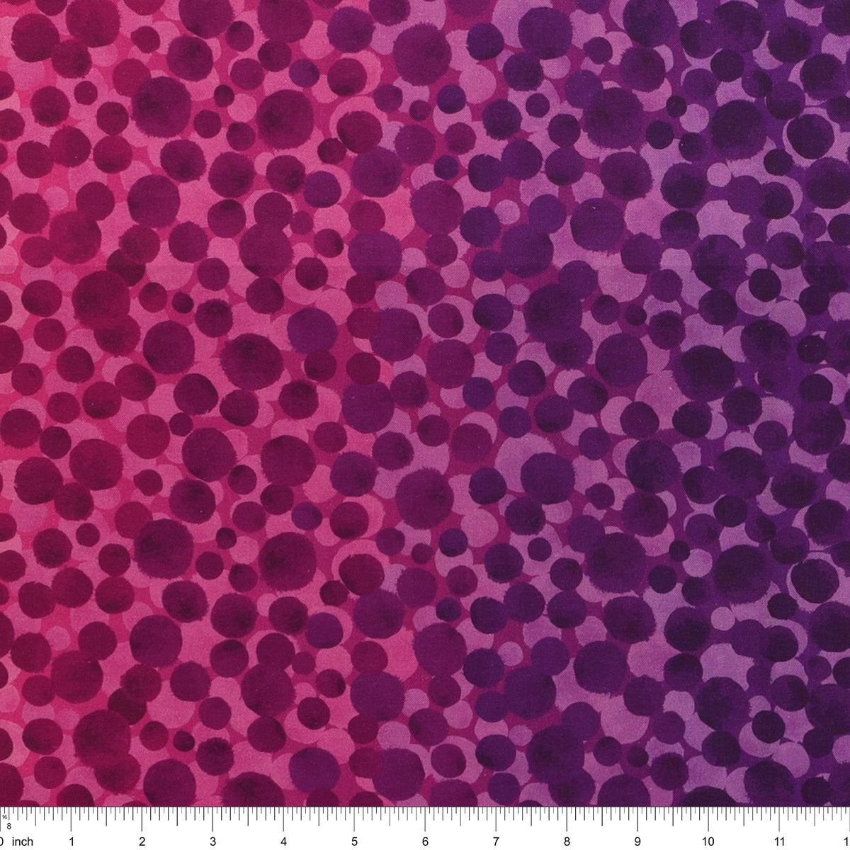 Bumbleberries Pinky Purple fabric with irregular dots in shades of magenta, plum, and violet over a pink-to-purple gradient background with a ruler for scale. 