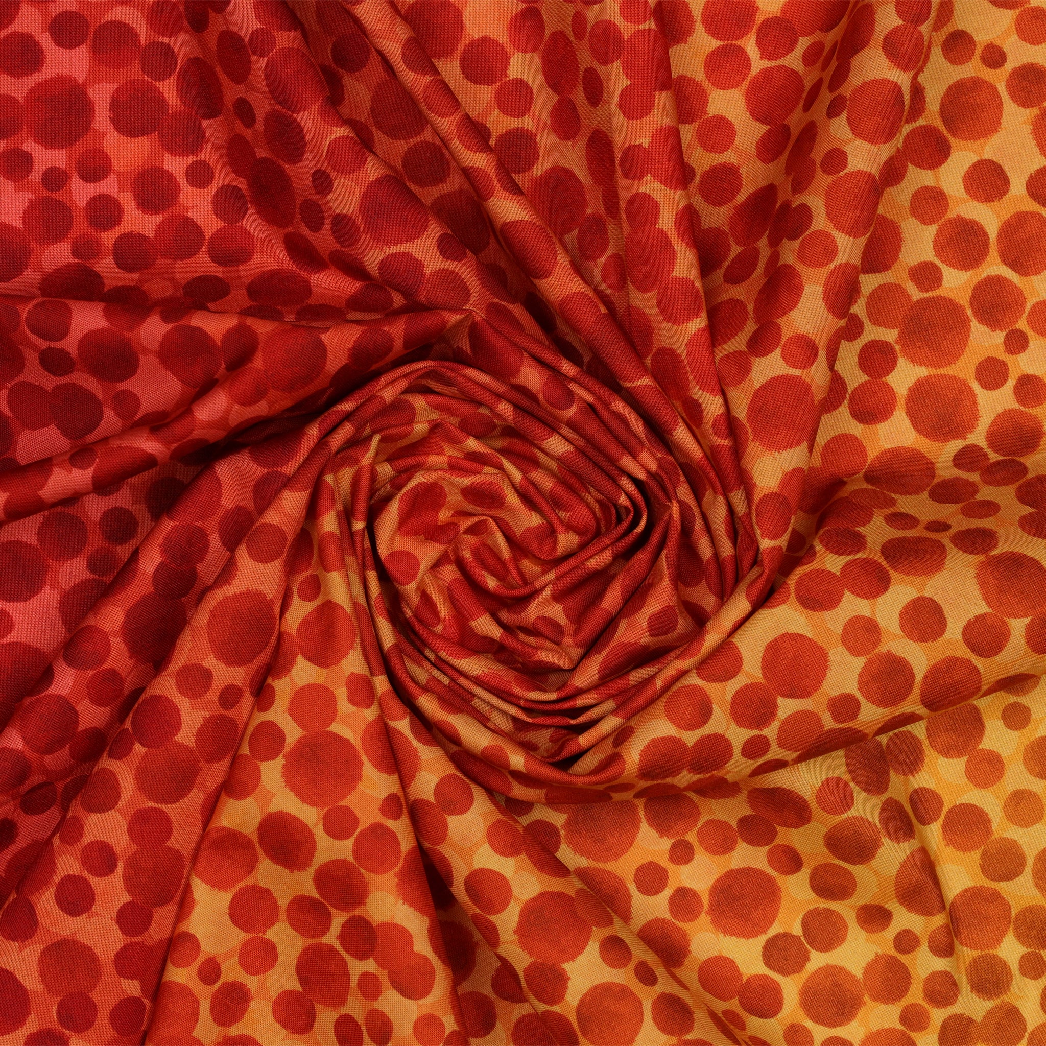 Bumbleberries Flame fabric gathered in a spiral, showcasing red and orange watercolor-style dots on a warm yellow background.