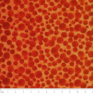 Bumbleberries Flame fabric with irregular red and rust-colored dots in varying sizes against a bright orange background and a ruler for scale. 