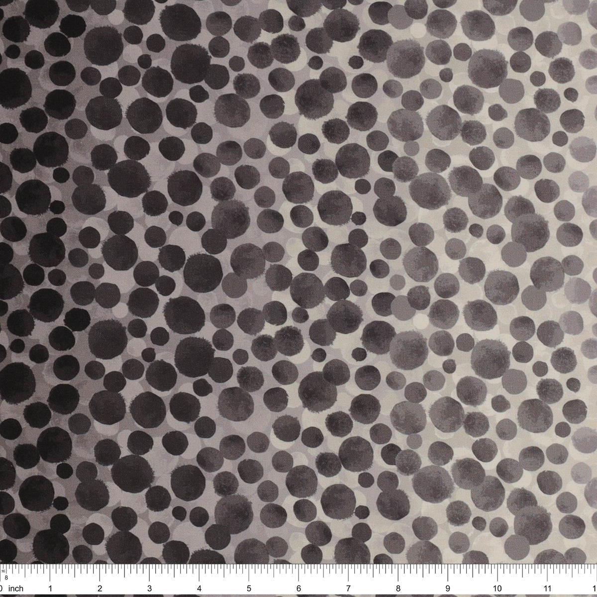 Bumbleberries Black to White fabric with a dense dotted pattern that gradually transitions from black along the edges to lighter gray and white toward the center, ruler for scale.