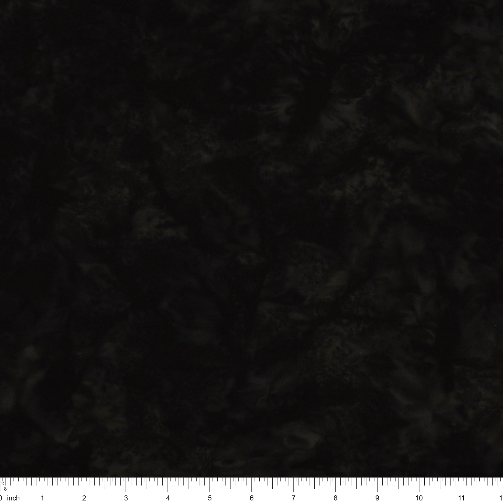 A close-up of a dark, mottled fabric texture with a white inch ruler along the bottom edge for scale.