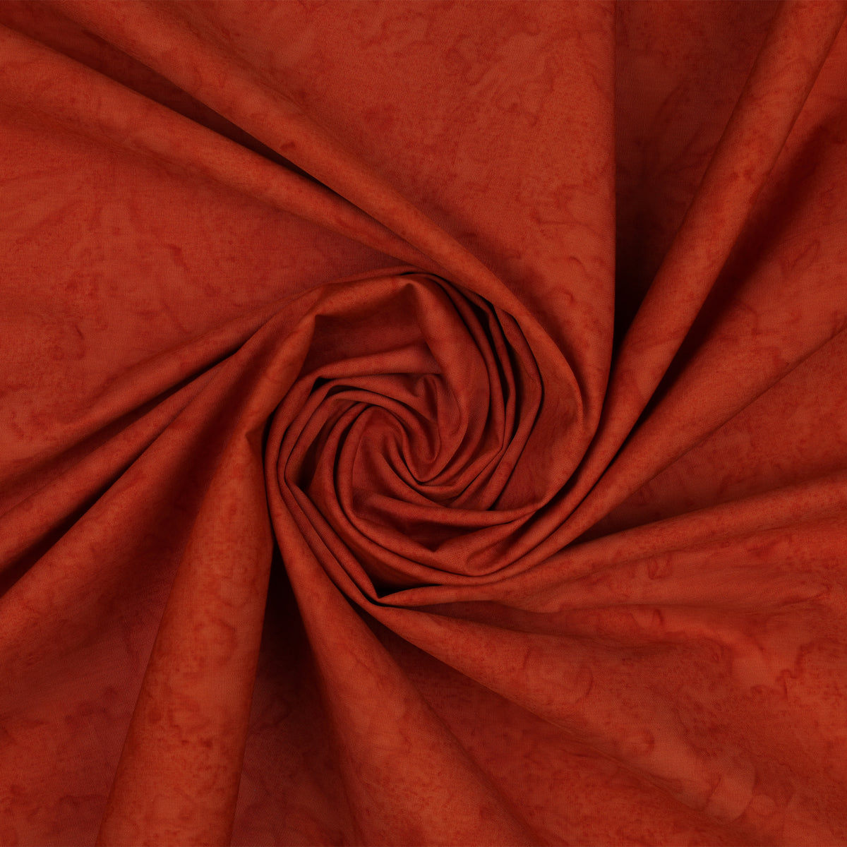 A close-up of draped fabric in a warm rust or burnt orange color, arranged in a spiral fold pattern.