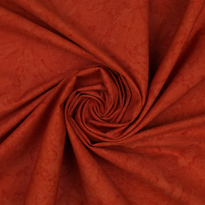 A close-up of draped fabric in a warm rust or burnt orange color, arranged in a spiral fold pattern.