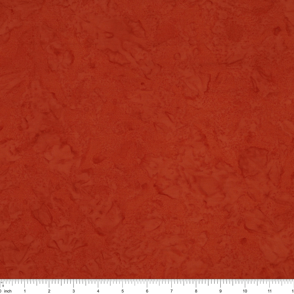 A close-up of a textured terracotta or rust-colored fabric, showing a mottled, slightly distressed surface. A white ruler with black markings is visible along the bottom edge to indicate scale.