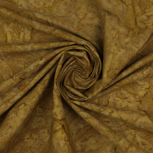 A close-up of draped fabric with a mottled, marbled pattern in warm golden brown, tan, and olive tones, arranged in a spiral fold.